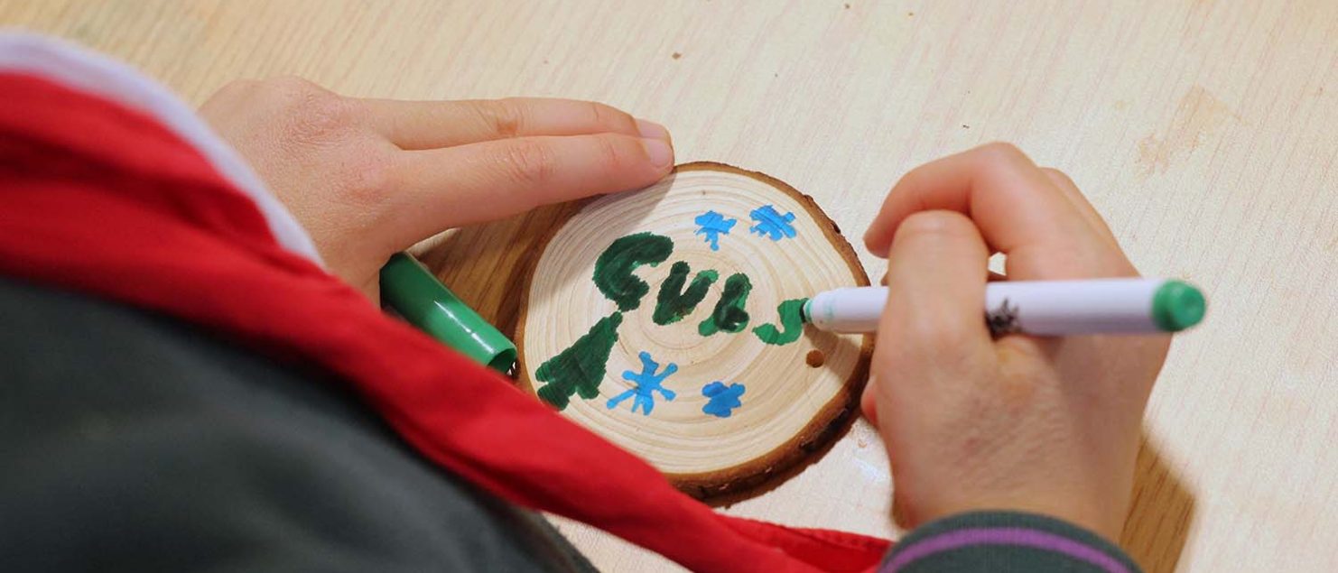 A cub draws a Christmas scene and writes 'Cubs' on a wooden disc